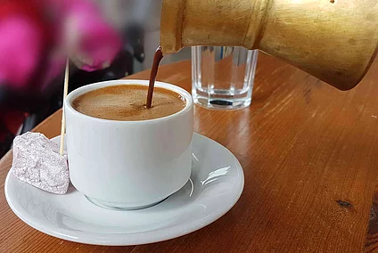 Coffee is poured from a small moka pot into a cup.
