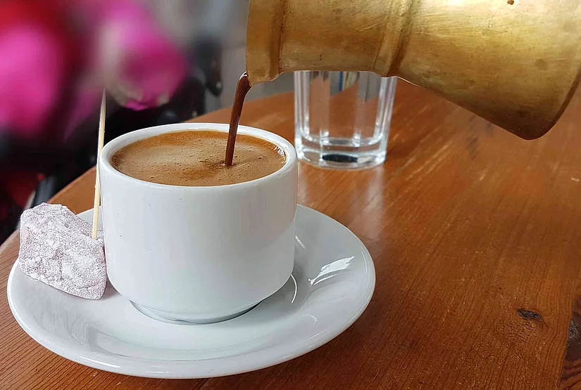 Coffee is poured from a small moka pot into a cup.